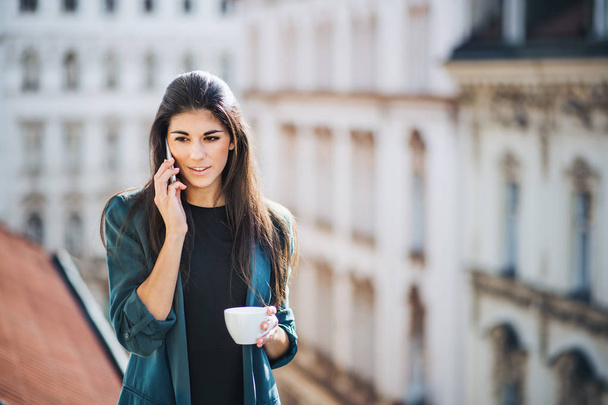 Молода бізнес-леді зі смартфоном, що стоїть на терасі біля офісу в місті
. - Фото, зображення