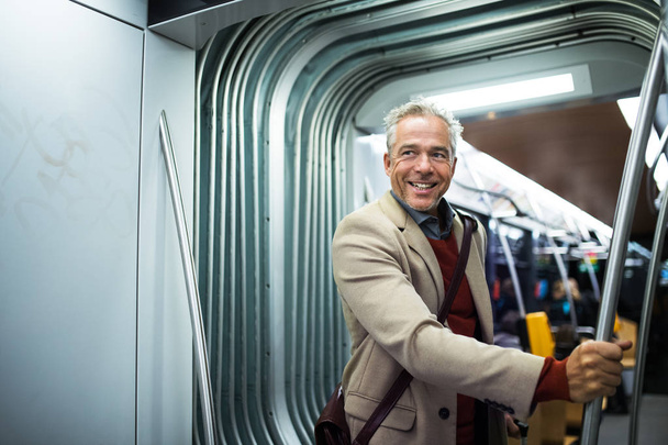 Mature businessman with smartphone travelling by tram in city. - Foto, Imagem