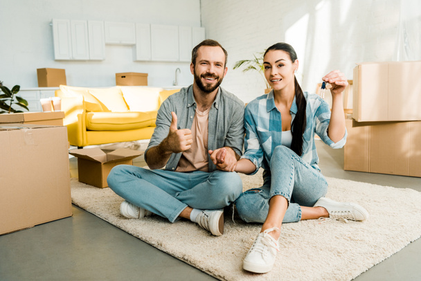 husband doing thumbs up sign while wife holding keys from new house, moving concept - Photo, Image