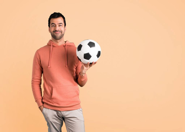 Man in a pink sweatshirt with soccer ball on ocher background - Photo, Image