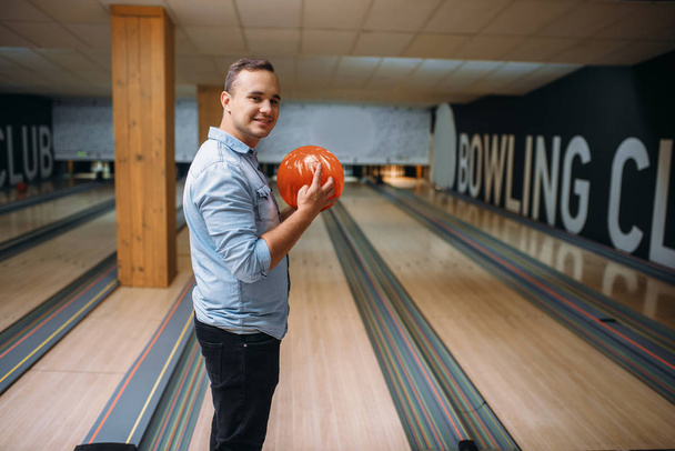 Male bowler standing on lane and poses with ball in hands, back view. Bowling alley player prepares to throw strike shot in club, active leisure - 写真・画像