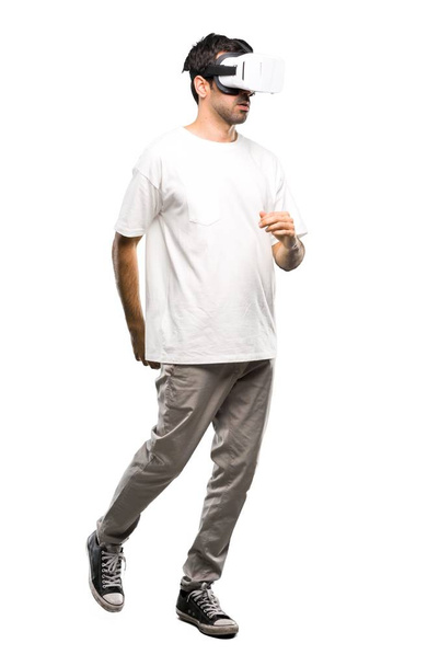 Ένα ολόσωμο πυροβολισμό ενός άνδρα που χρησιμοποιείτε Vr γυαλιά περπάτημα. Κίνηση σε απομονωμένες άσπρο φόντο - Φωτογραφία, εικόνα