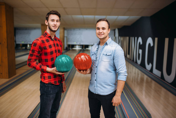 Two male bowlers poses on lane with balls on hands. Bowling alley players before competition. Classical tenpin game in club, active leisure - Fotó, kép