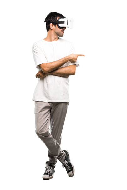 Um tiro de comprimento total de um homem usando óculos VR apontando o dedo para o lado em fundo branco isolado
 - Foto, Imagem