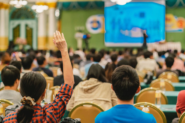 Vue arrière de l'auditoire montrant la main pour répondre à la question du Président sur la scène dans la salle de conférence ou réunion de séminaire, concept d'affaires et d'éducation
 - Photo, image