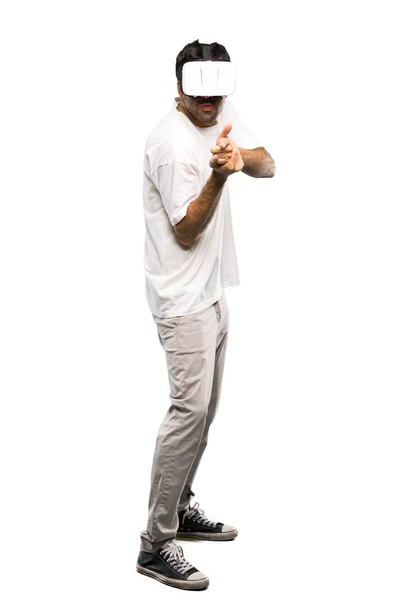 A full-length shot of a Man using VR glasses shooting with a virtual pistol on isolated white background - Photo, Image