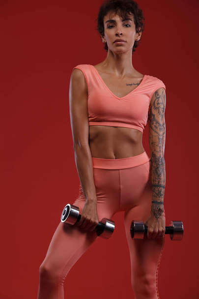 Fit woman athlete holding dumbbell . Fitness and motivation concept. Red background. - Fotoğraf, Görsel