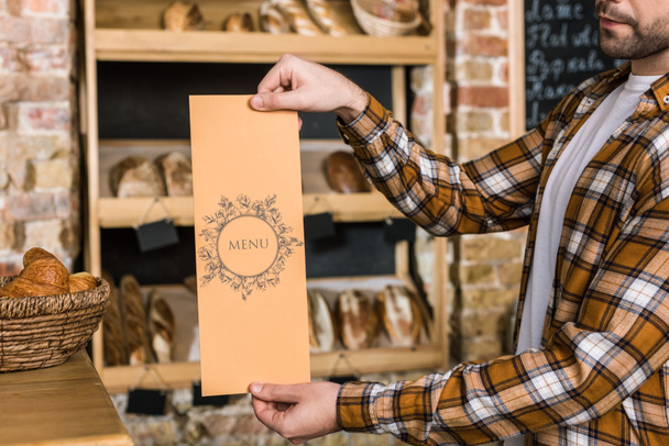 vendedor masculino segurando menu de papel nas mãos na padaria
 - Foto, Imagem