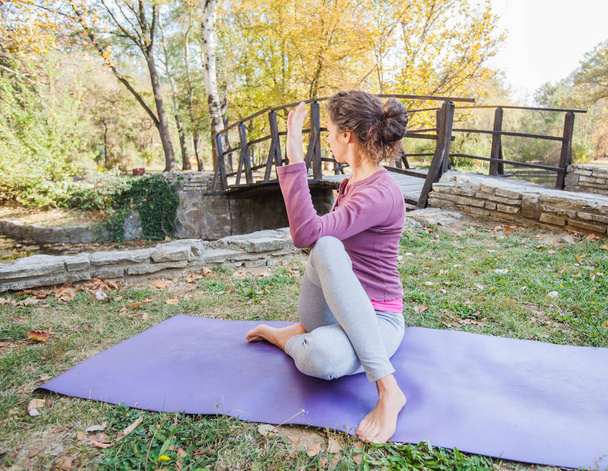 sportliche junge Frau beim Yoga, ardha matsyendrasana, sitzend halb Wirbelsäulendrehung, halb Herr der Fische, im Park. - Foto, Bild