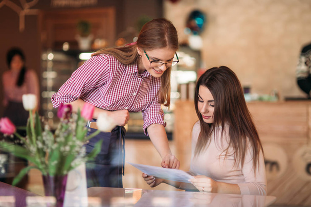 Hospitable waitress help to customer what to choose something from menu - Foto, imagen