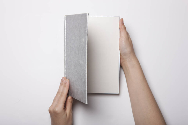 Рука жінки тримає порожню книгу, розкладену на білому столі
 - Фото, зображення