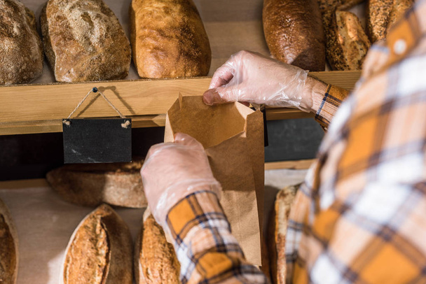 cropped view of male hands putting bread in paper bag - Foto, imagen