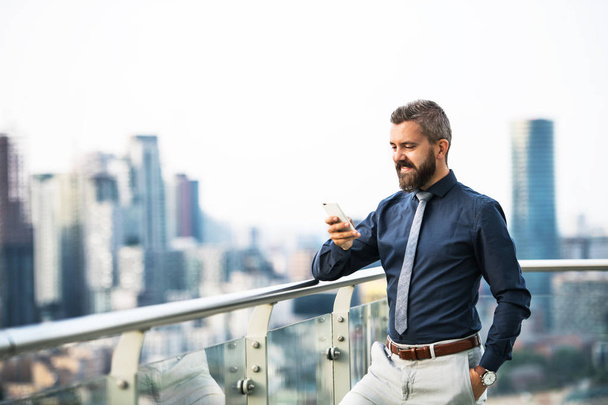 A portrait of businessman with smartphone standing against London view panorama. - Foto, afbeelding