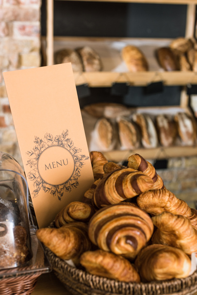 close up of fresh baked croissants in wicker basket with menu  - Foto, Imagem