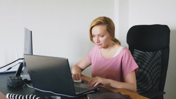 όμορφη νεαρή γυναίκα που εργάζεται σε ένα φορητό υπολογιστή και υπολογιστή ενώ κάθεται σε ένα γραφείο. - Πλάνα, βίντεο