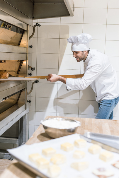 concentrated baker taking out hot bread from oven at kitchen - Foto, afbeelding