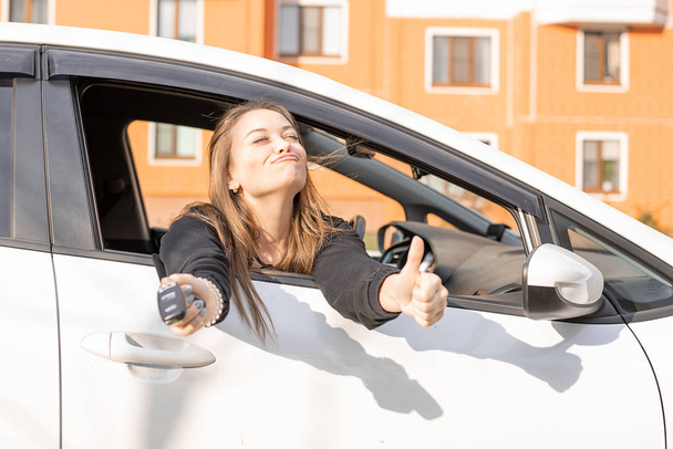Menina bonita jovem olha para fora da janela do carro, nas mãos de suas chaves do carro, compra feliz
 - Foto, Imagem