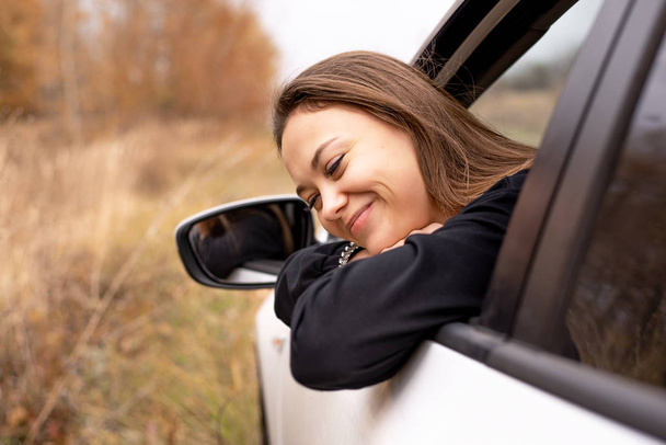 Krásná mladá dívka v podzimní den sedí v autě, při pohledu z okna řidiče - Fotografie, Obrázek