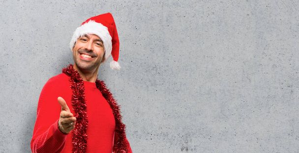 Man with red clothes celebrating the Christmas holidays shaking hands for closing a good deal on textured background - Фото, изображение