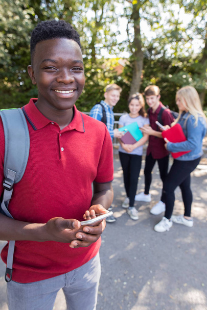 Retrato de un estudiante de secundaria adolescente al aire libre con amigos sosteniendo el teléfono móvil
 - Foto, imagen