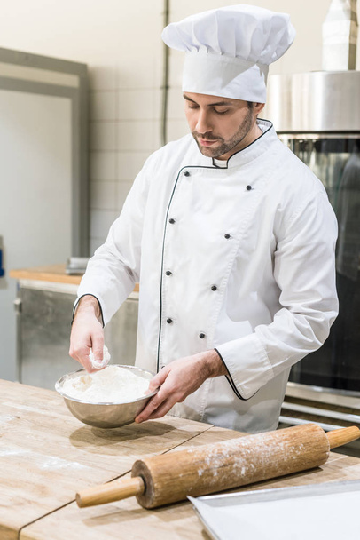 adult male baker scattering flour on wooden board at kitchen - Zdjęcie, obraz