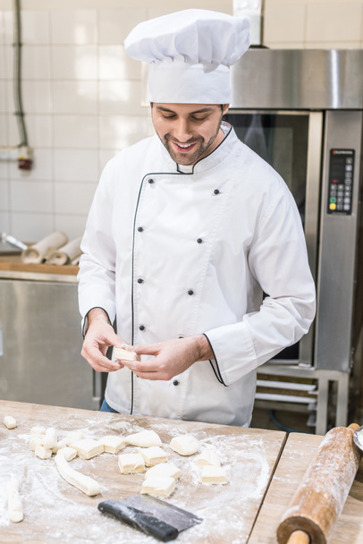 Smiling baker with uncooked dough at professional kitchen - Valokuva, kuva