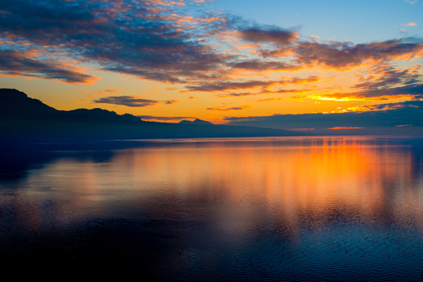 Hermosa puesta de sol colorida en otoño con siluetas de los Alpes franceses y fantásticos colores naranjas brillantes reflejados en el lago de Ginebra, Suiza
. - Foto, Imagen