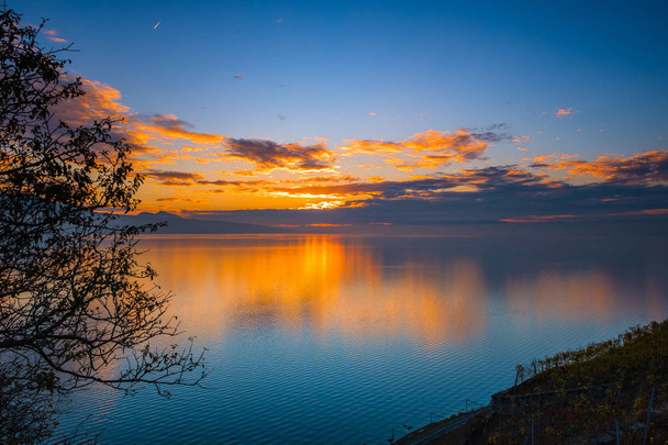 Πολύχρωμο ηλιοβασίλεμα το φθινόπωρο με σιλουέτες των γαλλικών Άλπεων και φανταστική πορτοκαλί λαμπερό αντανακλάται χρώματα η λίμνη της Γενεύης, Ελβετία. - Φωτογραφία, εικόνα
