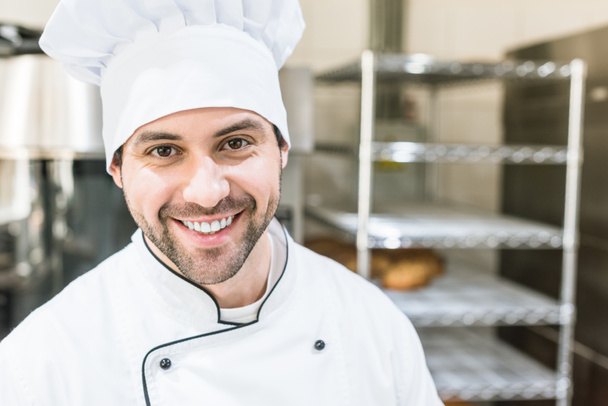 Handsome cook in chefs uniform smiling in bakehouse  - Foto, imagen
