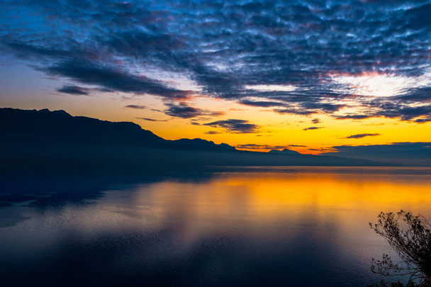 Beau coucher de soleil coloré en automne avec des silhouettes des Alpes françaises et de fantastiques couleurs orangées réfléchies sur le lac Léman, Suisse
. - Photo, image