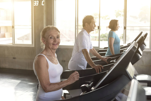 Spor salonundaki kıdemli koşucunun grup arkadaşı gülümsüyor ve mutlu. Yaşlı sağlıklı yaşam tarzı. - Fotoğraf, Görsel