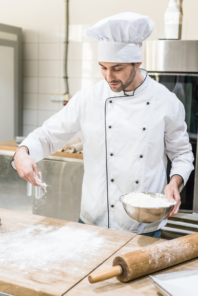 Baker in white chefs uniform cooking dough on wooden table - Foto, Bild