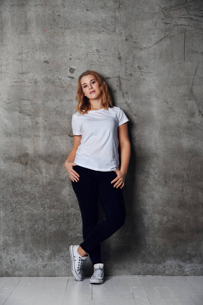 attractive young woman dressed in a white blank t-shirt posing against a background of a concrete wall - Фото, изображение