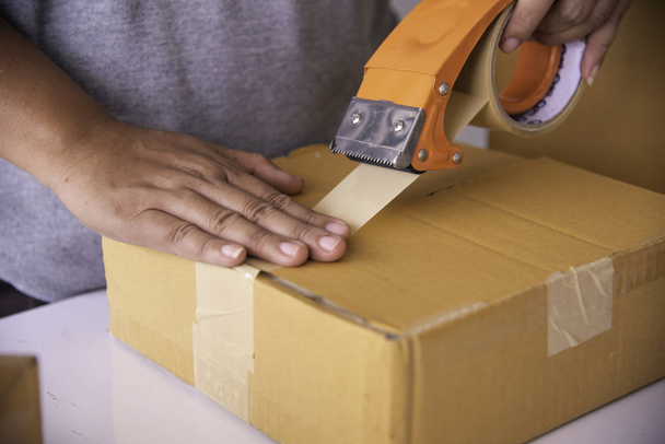 The staff is using the tape to pack the package goods to the customer. - Photo, Image