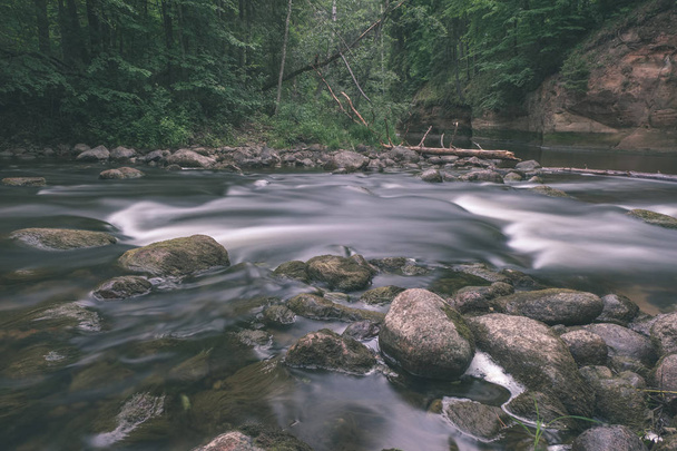 long exposure of beautiful rocky mountain river in summer with high water stream level in forest with trees and sandy foreground shore  - Photo, Image