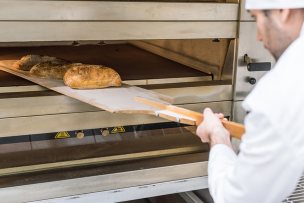 Bäcker holt frisch gebackenes Brot heraus  - Foto, Bild