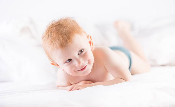 Habby young smilling child boy in white bed. - Zdjęcie, obraz