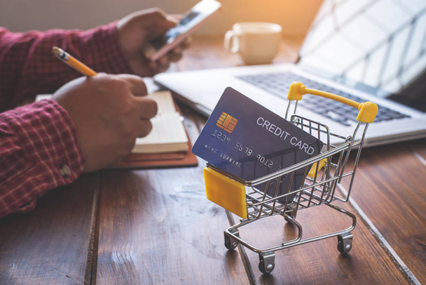 クレジットカードの内側と後ろの小さなショッピングカートは、デスク上のビジネスです-コンセプトは、ショッピングのためのクレジットを使用. - 写真・画像
