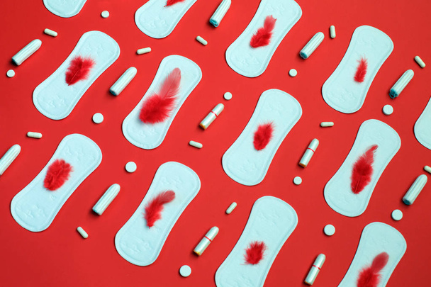 Piuma rossa e mucchio di assorbenti bianchi molti tamponi e pillole su sfondo rosso. Mestruazioni, mezzi di protezione dell'igiene
. - Foto, immagini