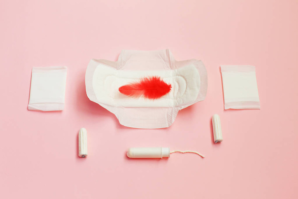 Červené pírko a hygienické vložky a savé listy na růžovém pozadí - Fotografie, Obrázek
