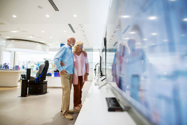 glückliches Seniorenpaar, das sich für einen Fernseher entscheidet. Innenausstattung eines Tech-Stores. - Foto, Bild