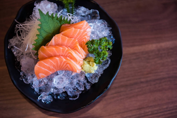 Zalm sashimi met plantaardige decoratie op ijs door bovenaanzicht. Japanse traditioneel voedsel met houten getextureerde achtergrond en kopie ruimte voor tekst. - Foto, afbeelding