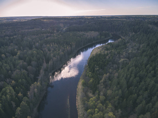Drohnenbild. Luftaufnahme des ländlichen Raums mit Feldern und Wäldern und Wasserspiegelungen im Fluss an bewölkten Frühlingstagen. Lettland - alter Film-Look - Foto, Bild