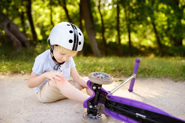 Toddler boy in safety helmet learning to ride scooter. Little child crashing during active outdoors game - Foto, Imagen