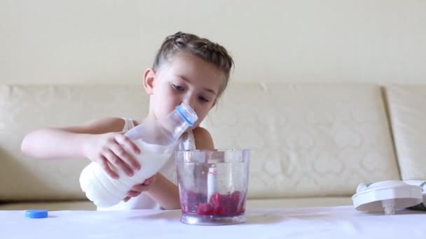 Baby gießt Milch in einen Mixer. Ein kleines Mädchen bereitet sich einen Cocktail zu, gießt Milch aus einer Glasflasche in die Schüssel eines Mixers. - Filmmaterial, Video
