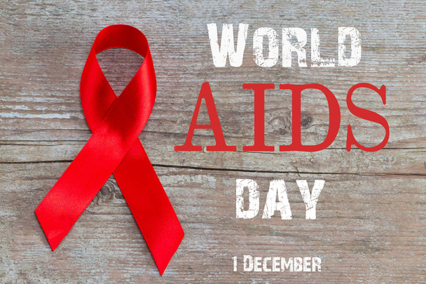 Red Ribbon - AIDS awareness symbol on the wooden background with text world AIDS day. - Фото, изображение