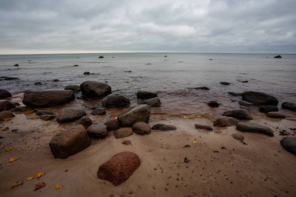 βραχώδη ακτή στη Λετονία με ροή νερού στη θάλασσα και μεγάλα βράχια στα τέλη του φθινοπώρου - Φωτογραφία, εικόνα