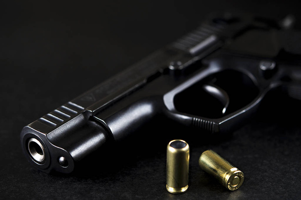 The black gun lies on a black background next to the patrons - Фото, зображення