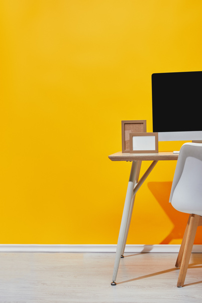 Počítač a prázdné rámečky na pracovišti žluté zdi - Fotografie, Obrázek