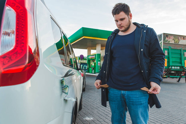 悲しい男は、ガソリン スタンドで空のポケットを示しています。車タンク概念ドルお金 - 写真・画像